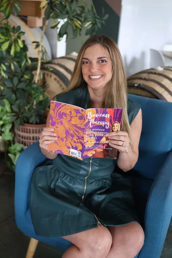 Kimberly Hogate smiling and holding her book Business Therapy: The Anxious Entrepreneur’s Quick Guide to Success