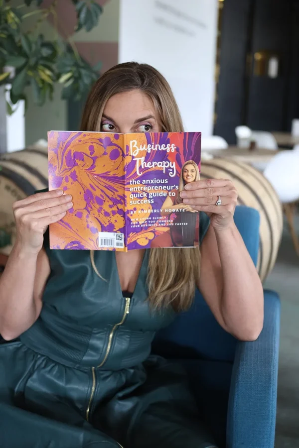 Kimberly Hogate peeking over the cover of her book Business Therapy