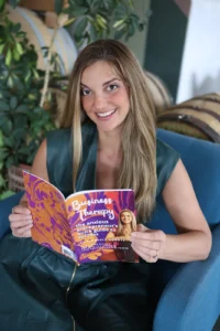 Kimberly Hogate reading her book Business Therapy in a blue armchair